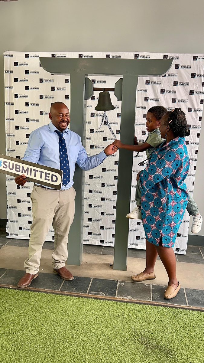 Brian and Manka ringing the bell together, holding a sign that reads Submitted.