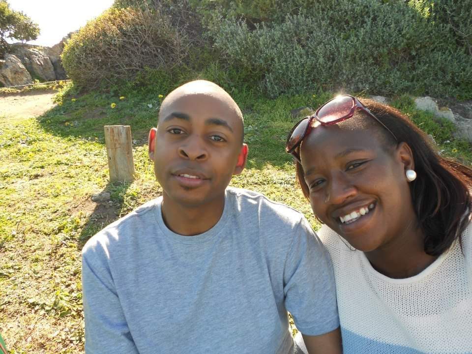Brian and Manka sitting together on a lawn in the sunshine.